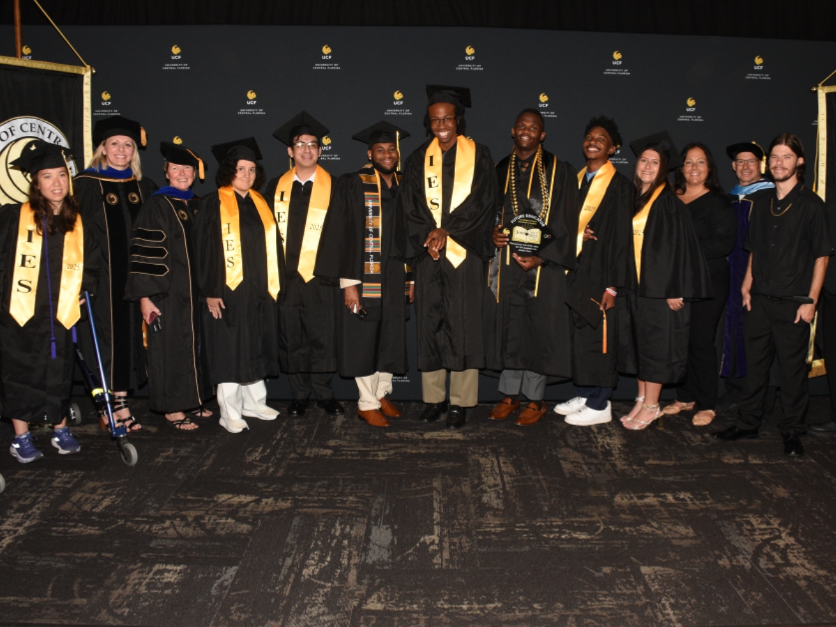 UCF graduates stand in caps and gowns wearing IEC stoles